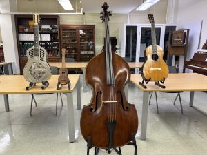 2 guitars, ukulele, and bass are shown on instrument stands