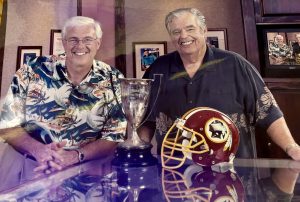 Photograph of radio personalities Michael Perry and Larry Price at a desk with a football helmet on it.