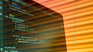 Green computer code words on a screen with orange rays of light coming out of the screen.